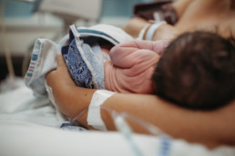 Photo of Newborn baby immediately after birth breastfeeding. You see the wrinkles in his newborn skin and his mother holding him