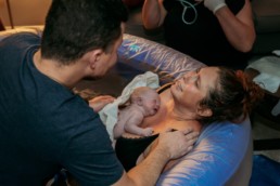 Newborn baby is on mother's chest. Mother and father look at each other moments after birth