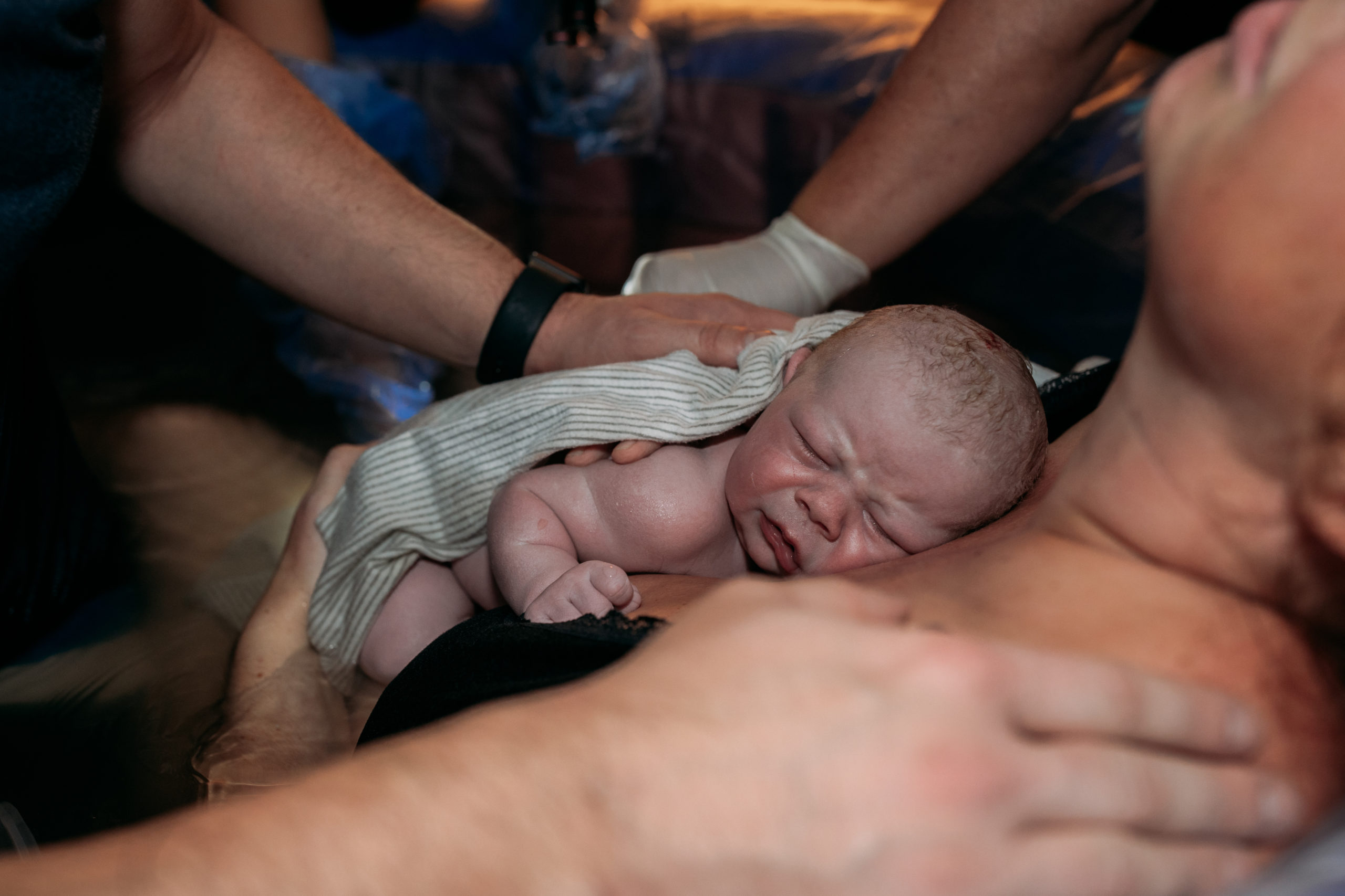 Hands of father, mother, and midwife support newborn baby who is on mother's chest shortly after childbirth in birth tub.