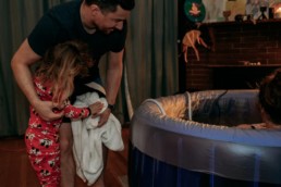 Father and sister look into birth tub at newborn baby