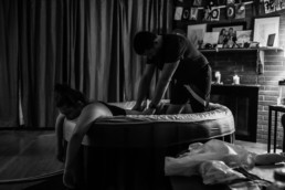 Photo captures dad supporting mom as she labors during childbirth at a home birth; Man applies counterpressure to womans back during a contraction in birth tub
