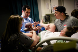 Photo of dad looking shocked at newborn baby at the time of birth while doctor holds baby up for him to see