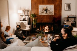 Mothers sit in circle around a fireplace. One mother holds a newborn baby