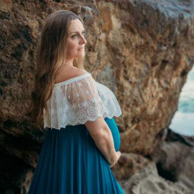 Pregnant women next to dramatic rock looking away from camera while holding belly