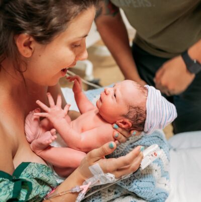 Mom in hospital gown hold newborn baby. Mom and baby look at each other in the eyes.