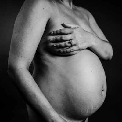 Image of pregnant bare belly. Mother drapes her arm across her body