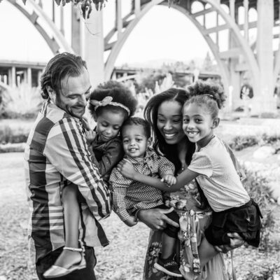 Image of a family of five hugging. Mom is holding two children while dad is holding one child. Everyone is in motion and smiling.