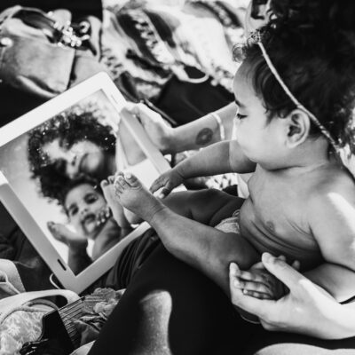 Black and white image of mother and baby looking into a mirror, their reflection shows their faces