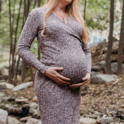 Pregnant woman stands in the woods holding her belly in her hands