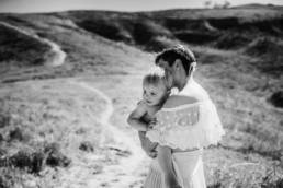 Black and white image of mother holding toddler in a hug amongst rolling hills