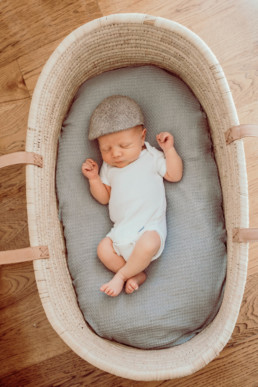 Photo of baby laying in a moses bakset asleep. Photo taken from above baby.