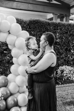 Black and white image of mother holding toddler on her hip. Child is holding mothers face with both hands and they look at each other.