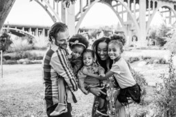 Image of a family of five hugging. Mom is holding two children while dad is holding one child. Everyone is in motion and smiling.