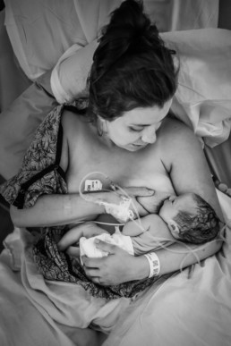 Photo of mom in hospital gown breastfeeding newborn baby. Visable is her iv line in her hand. Baby gazes up at mom.