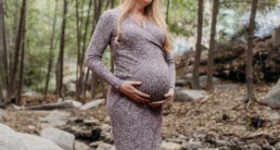 Pregnant woman stands in the woods holding her belly in her hands
