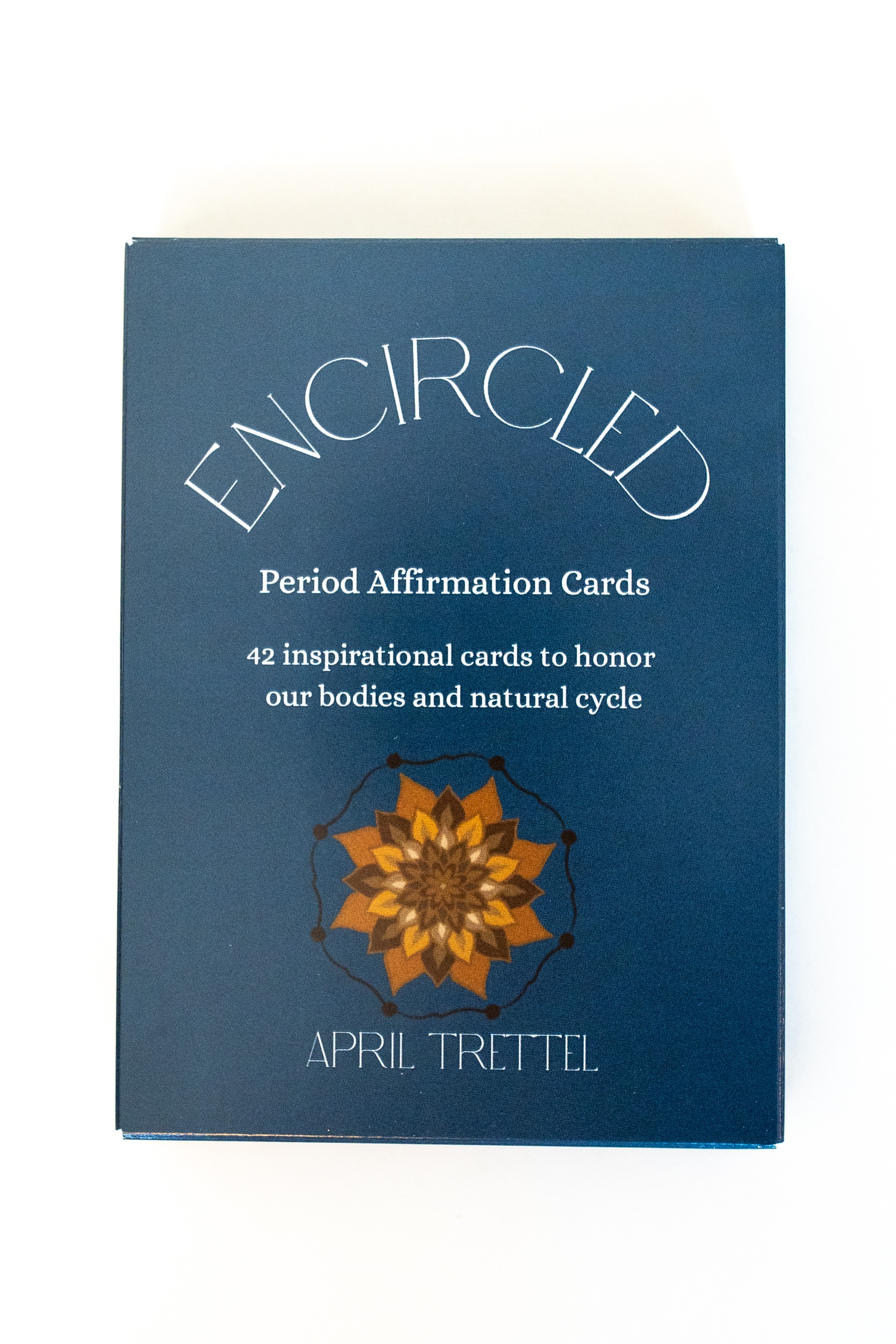 Photo of affirmation card deck entitled Encircled - period affirmation cards. Dark blue deck with golden flower pictured on the front